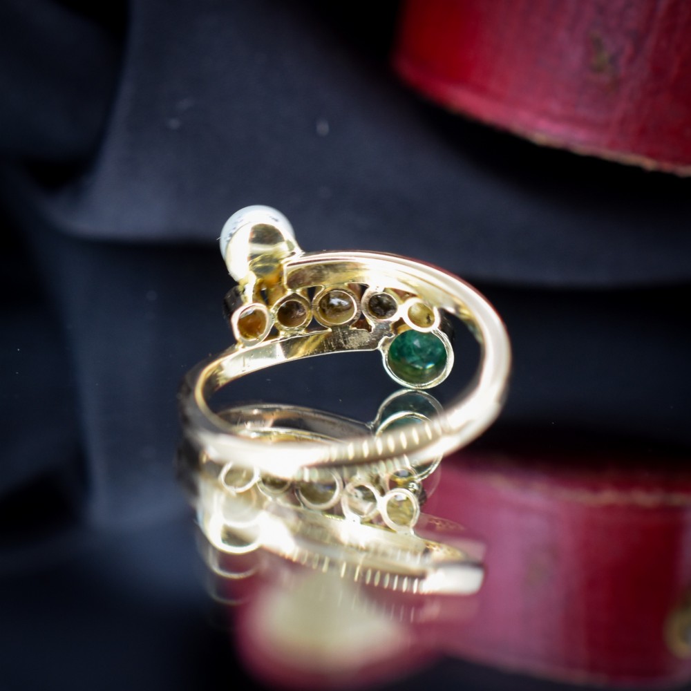A 14ct yellow gold bypass twist ring set with a single pearl, a round green emerald, and five bezel-set diamonds across the band. View IV
