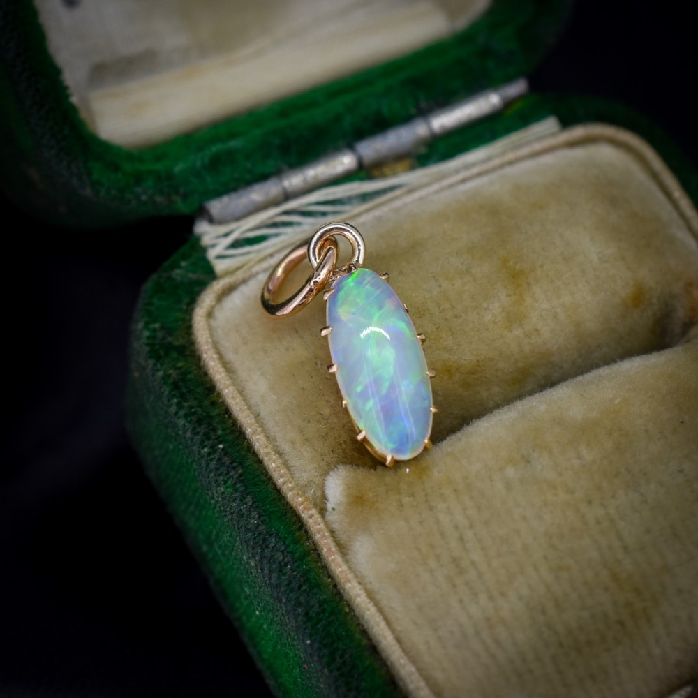 An oval natural opal cabochon pendant held in a multi-claw yellow gold setting with an attached jump ring.