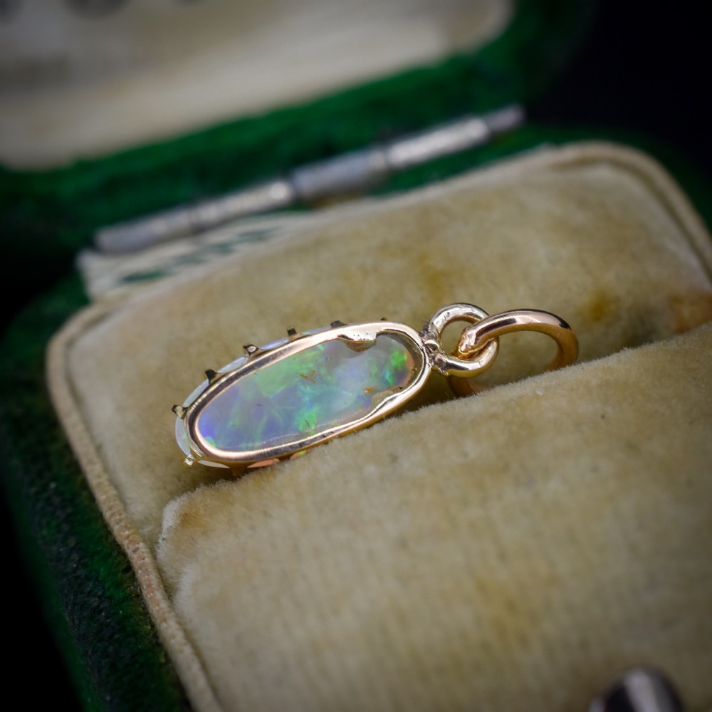 An oval natural opal cabochon pendant held in a multi-claw yellow gold setting with an attached jump ring. View IV
