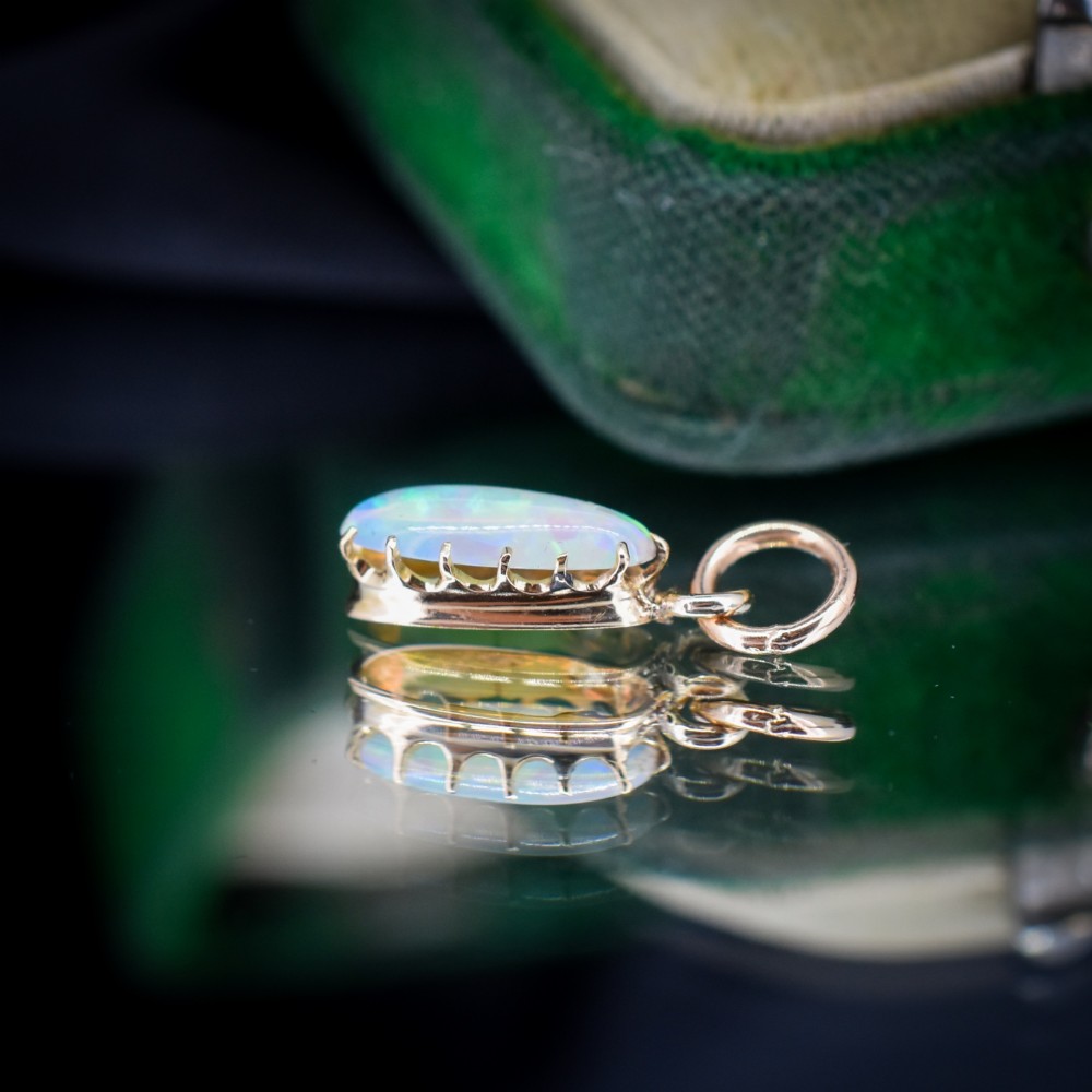 An oval natural opal cabochon pendant held in a multi-claw yellow gold setting with an attached jump ring. View V