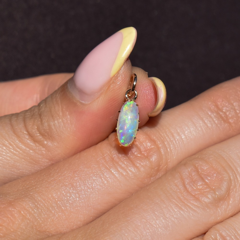 An oval natural opal cabochon pendant held in a multi-claw yellow gold setting with an attached jump ring. View VI