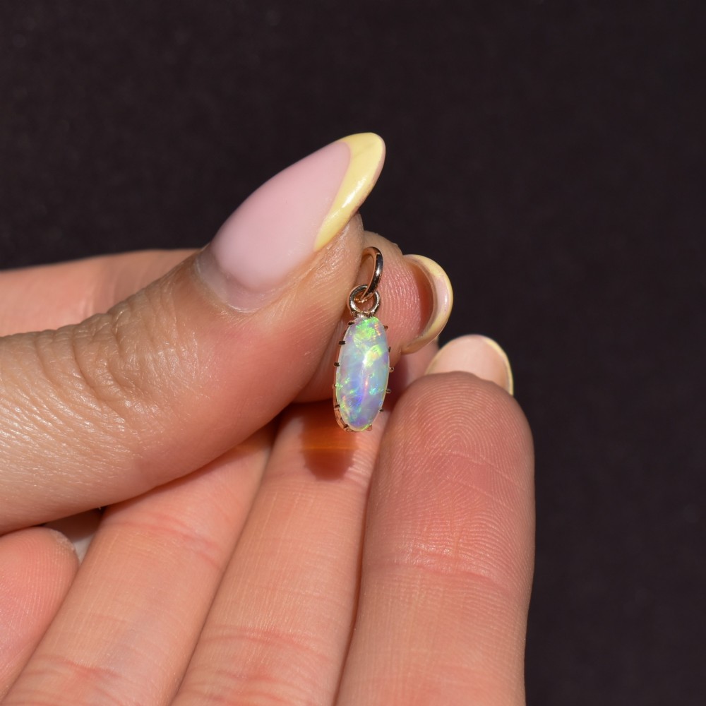 An oval natural opal cabochon pendant held in a multi-claw yellow gold setting with an attached jump ring. View VII