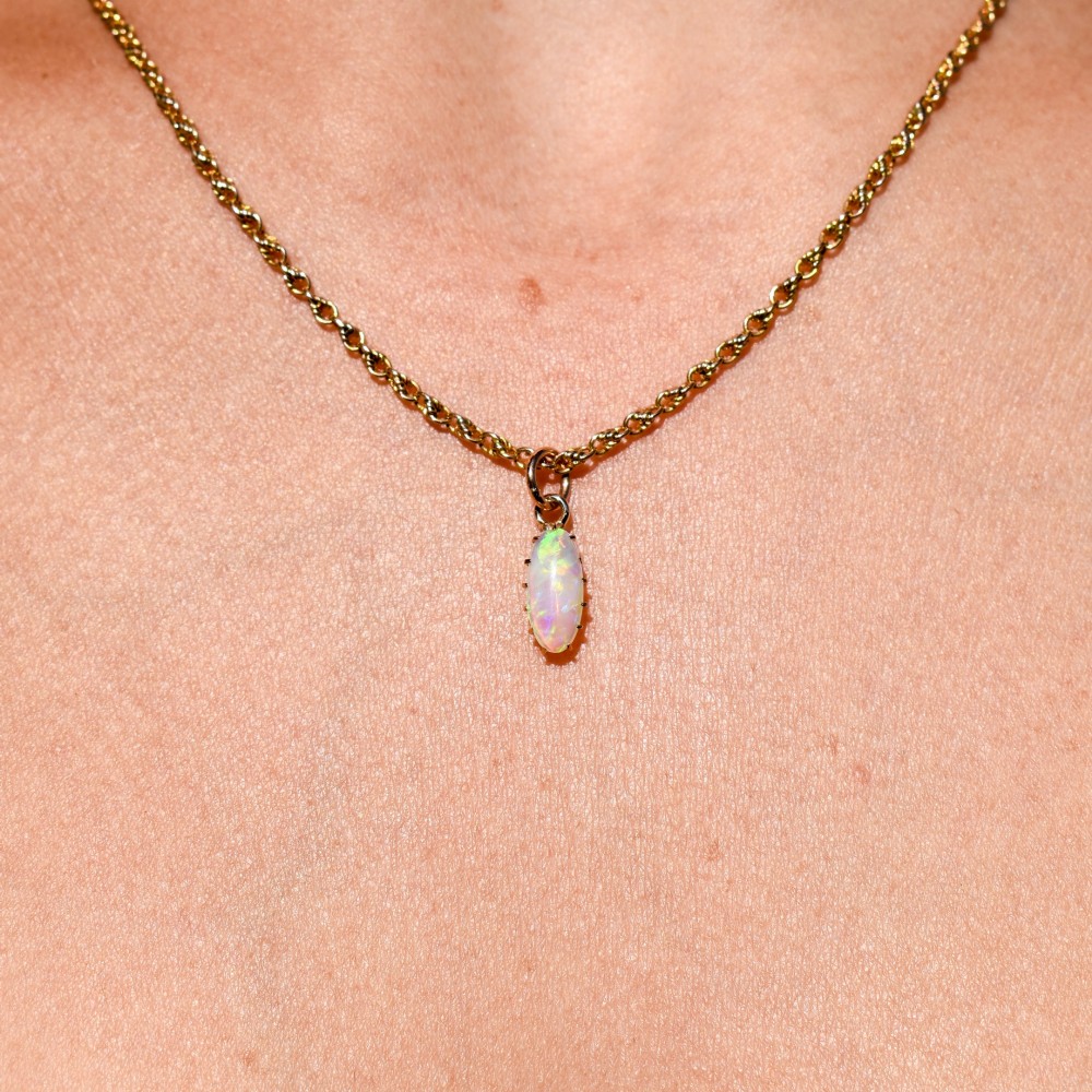 An oval natural opal cabochon pendant held in a multi-claw yellow gold setting with an attached jump ring. View VIII