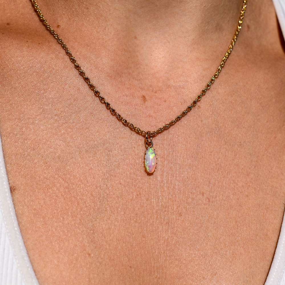 An oval natural opal cabochon pendant held in a multi-claw yellow gold setting with an attached jump ring. View IX