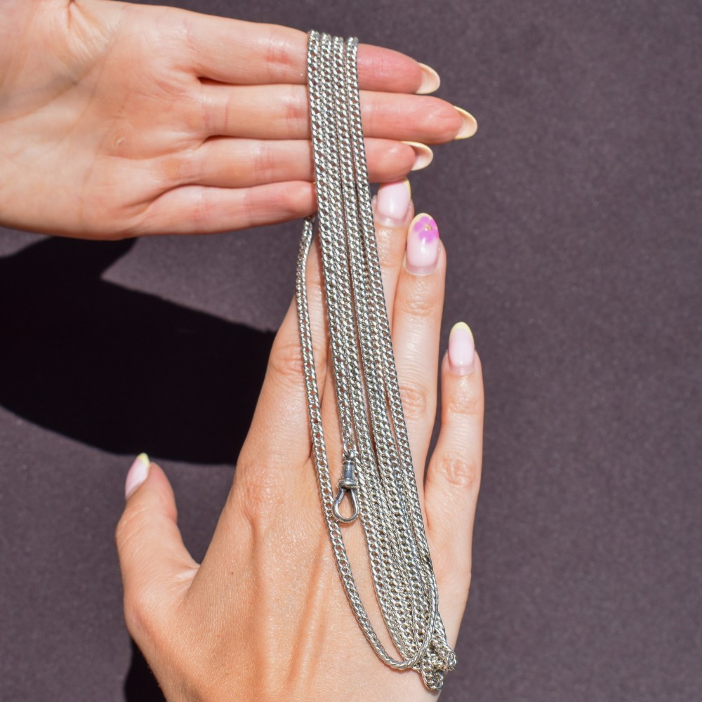 A long sterling silver flat curb link guard chain draped in multiple tiers with a dog clip clasp at the bottom. View XI