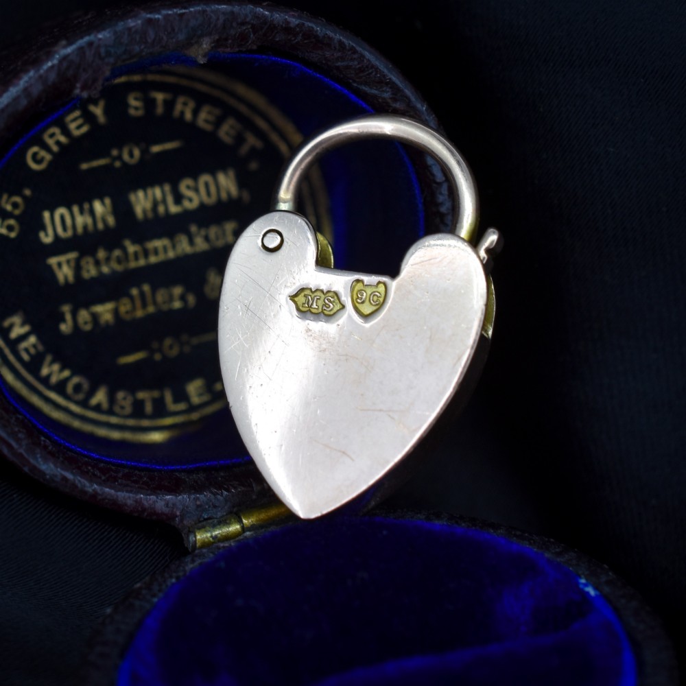 An antique 9ct gold heart-shaped padlock pendant with a smooth polished finish, central keyhole detail, and visible screw head accents. View IV