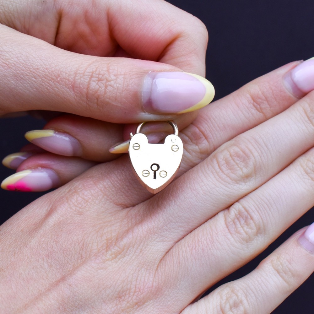 An antique 9ct gold heart-shaped padlock pendant with a smooth polished finish, central keyhole detail, and visible screw head accents. View VII