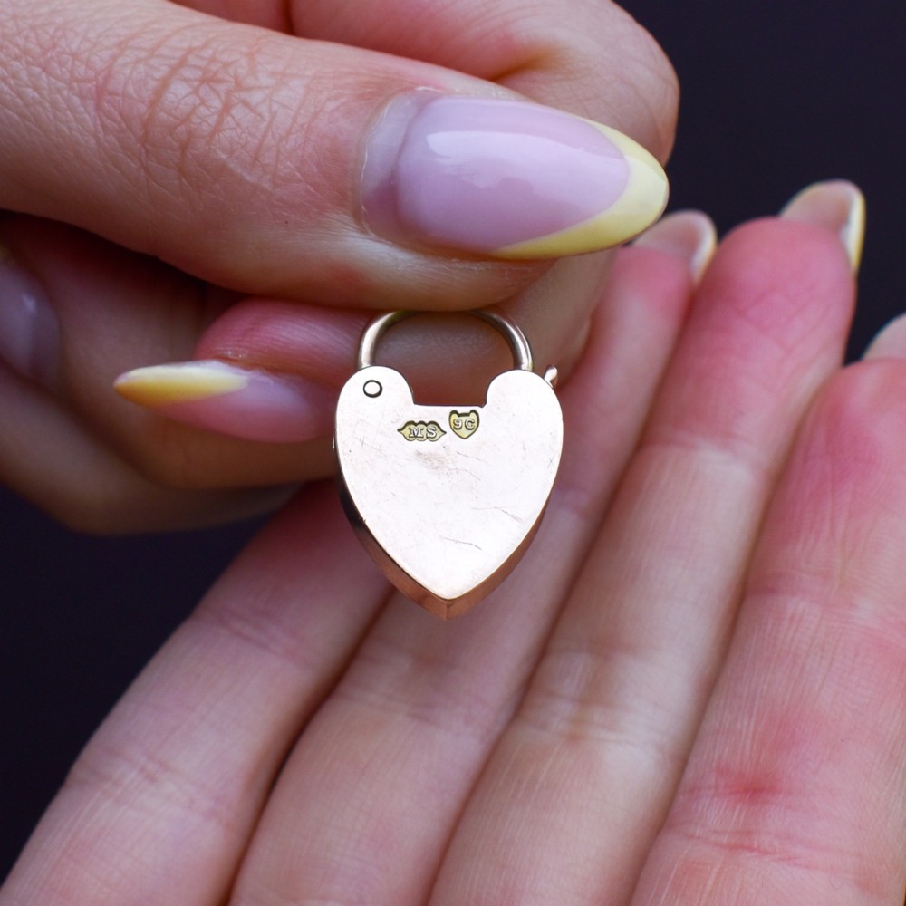 An antique 9ct gold heart-shaped padlock pendant with a smooth polished finish, central keyhole detail, and visible screw head accents. View VIII