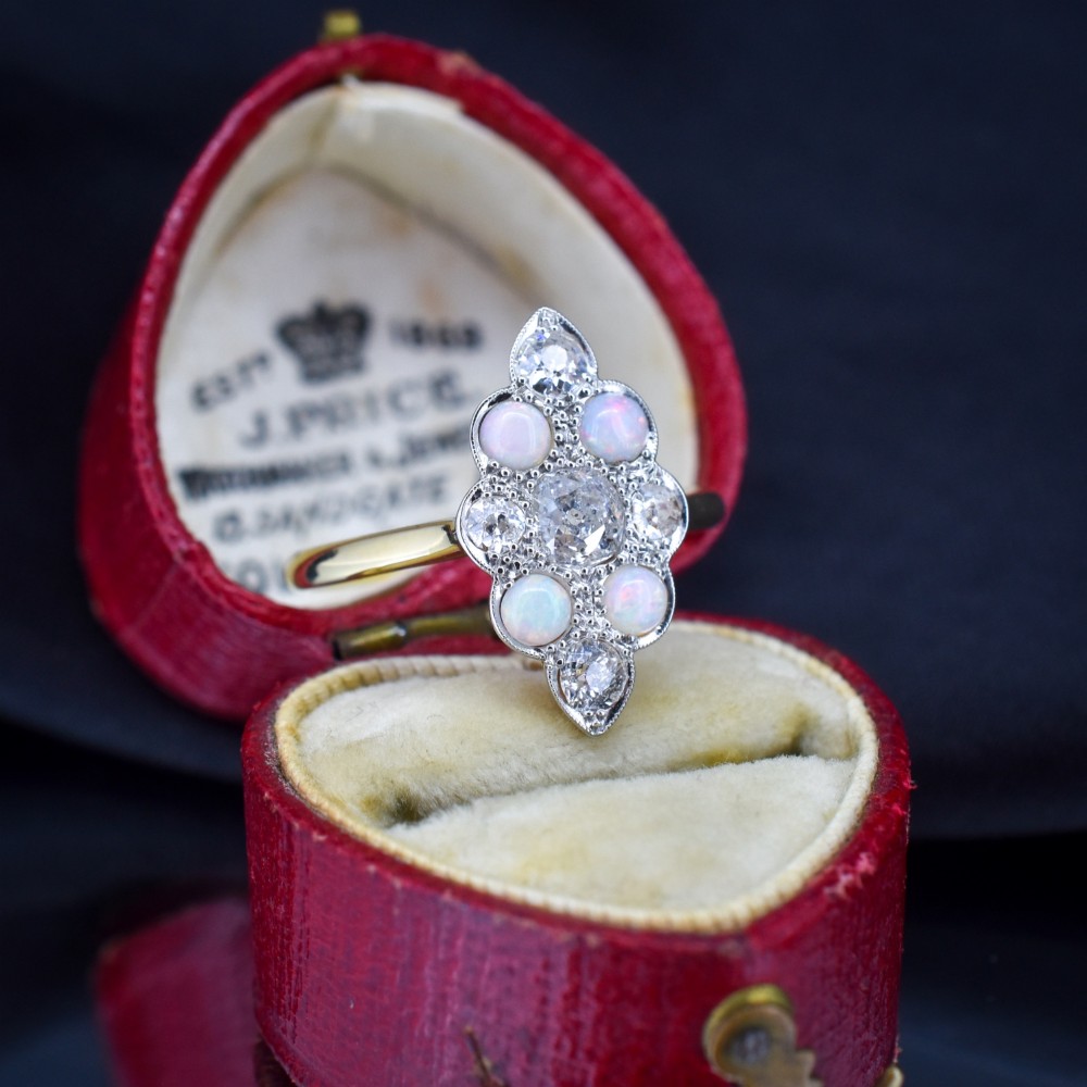 An Edwardian 18ct gold and platinum navette cluster ring featuring a central old cut diamond bordered by four cabochon opals and additional diamond accents.