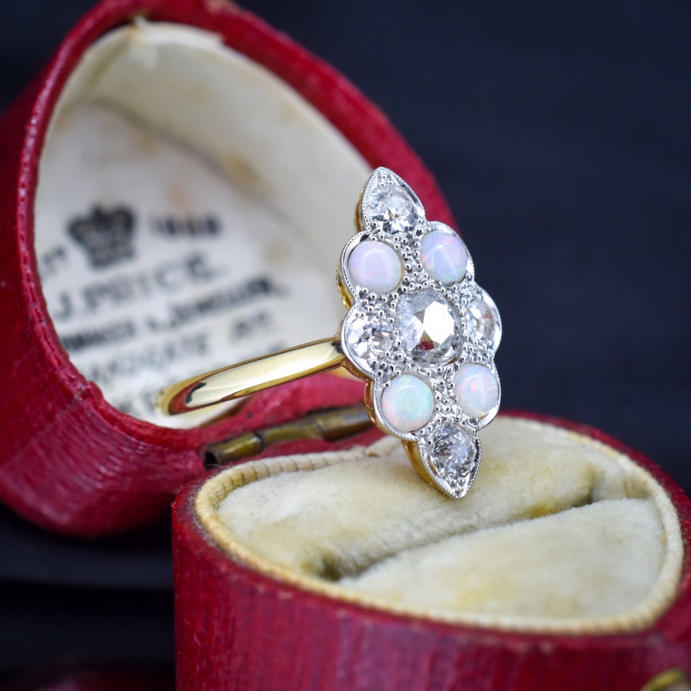 An Edwardian 18ct gold and platinum navette cluster ring featuring a central old cut diamond bordered by four cabochon opals and additional diamond accents. View II