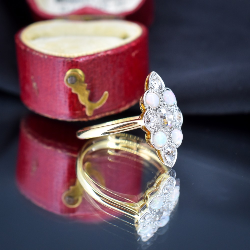 An Edwardian 18ct gold and platinum navette cluster ring featuring a central old cut diamond bordered by four cabochon opals and additional diamond accents. View V