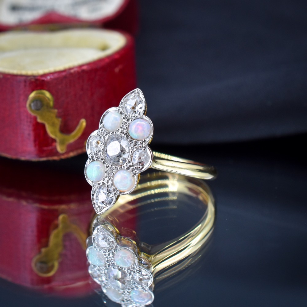An Edwardian 18ct gold and platinum navette cluster ring featuring a central old cut diamond bordered by four cabochon opals and additional diamond accents. View VII
