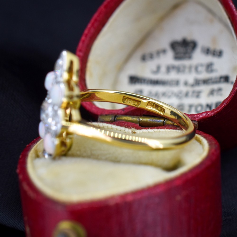 An Edwardian 18ct gold and platinum navette cluster ring featuring a central old cut diamond bordered by four cabochon opals and additional diamond accents. View VIII