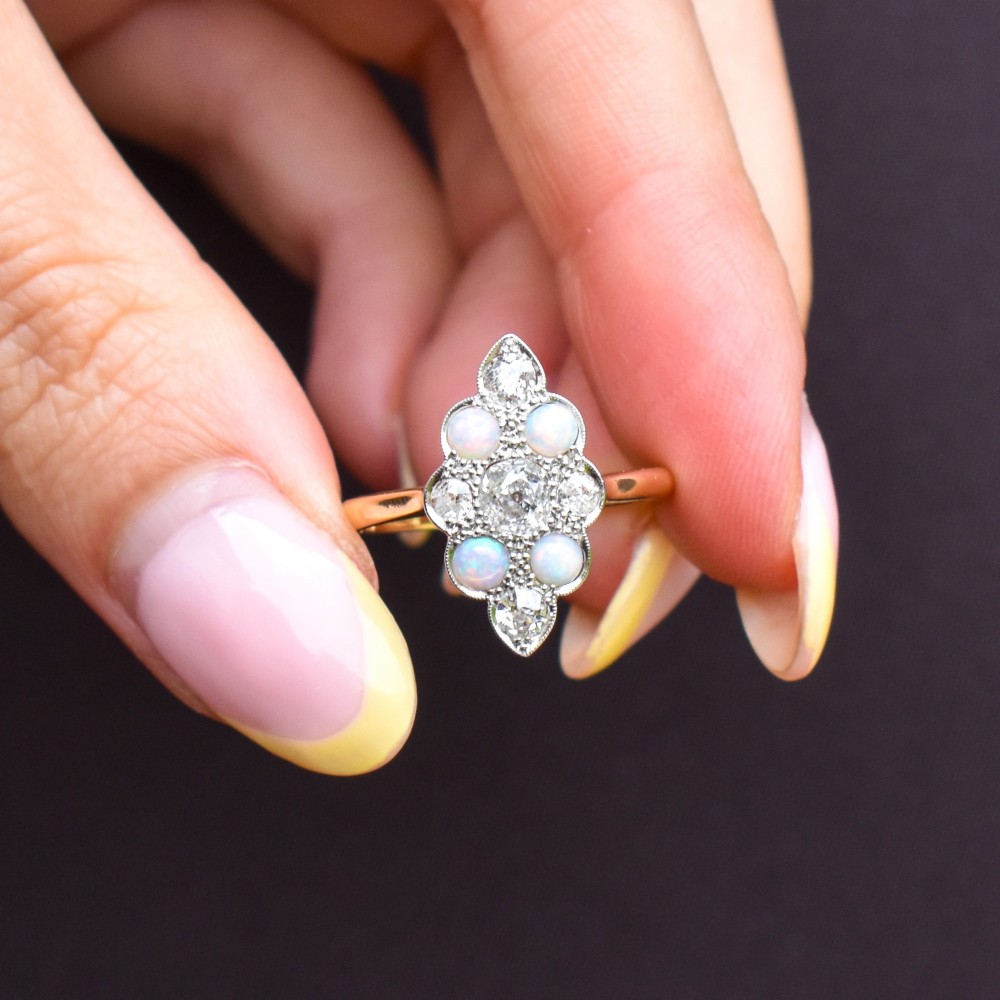 An Edwardian 18ct gold and platinum navette cluster ring featuring a central old cut diamond bordered by four cabochon opals and additional diamond accents. View IX
