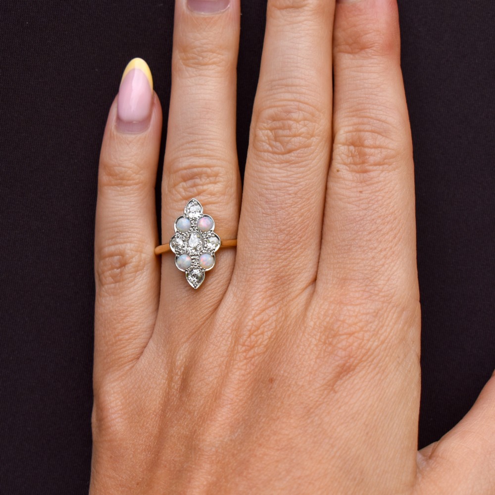 An Edwardian 18ct gold and platinum navette cluster ring featuring a central old cut diamond bordered by four cabochon opals and additional diamond accents. View XI