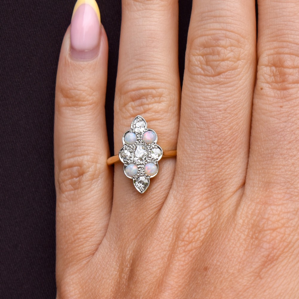 An Edwardian 18ct gold and platinum navette cluster ring featuring a central old cut diamond bordered by four cabochon opals and additional diamond accents. View XII