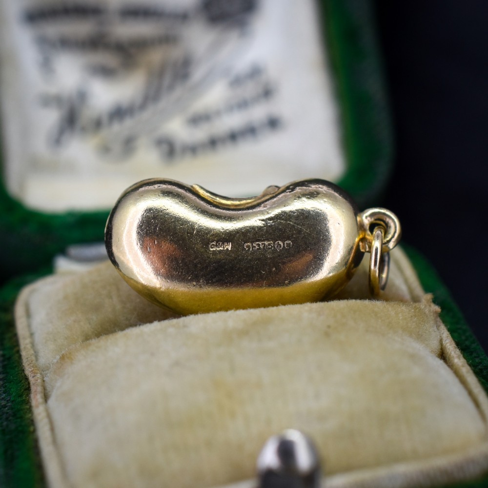 A smooth, polished 9ct yellow gold bean-shaped charm with an attached suspension jump ring. View IV