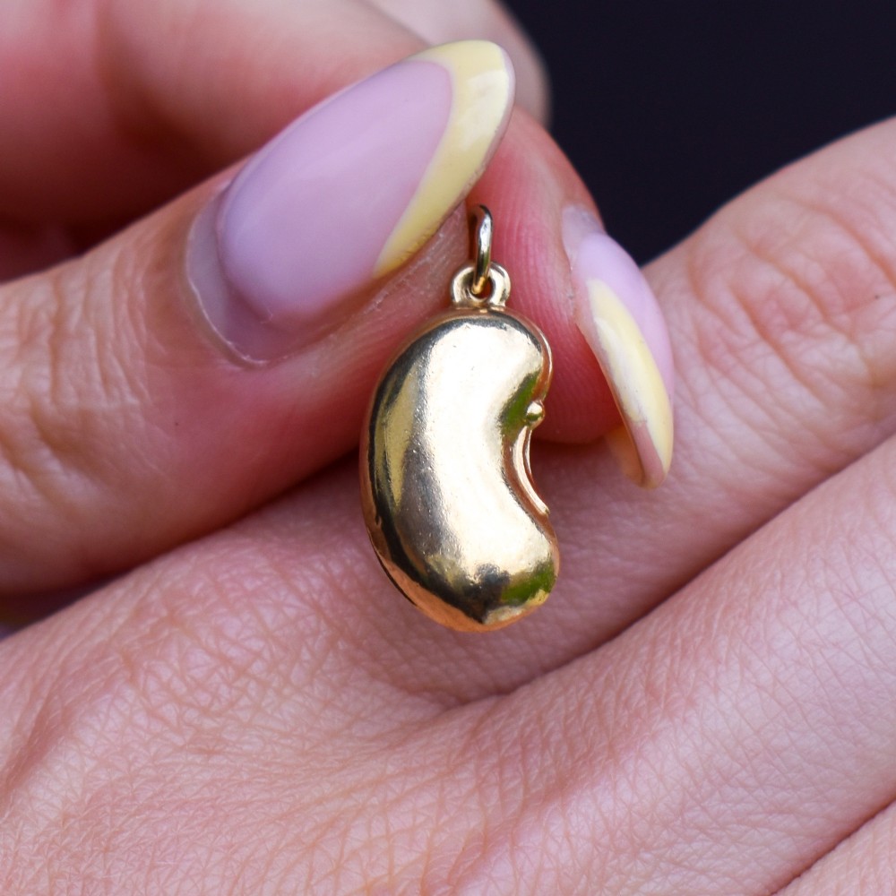A smooth, polished 9ct yellow gold bean-shaped charm with an attached suspension jump ring. View VII