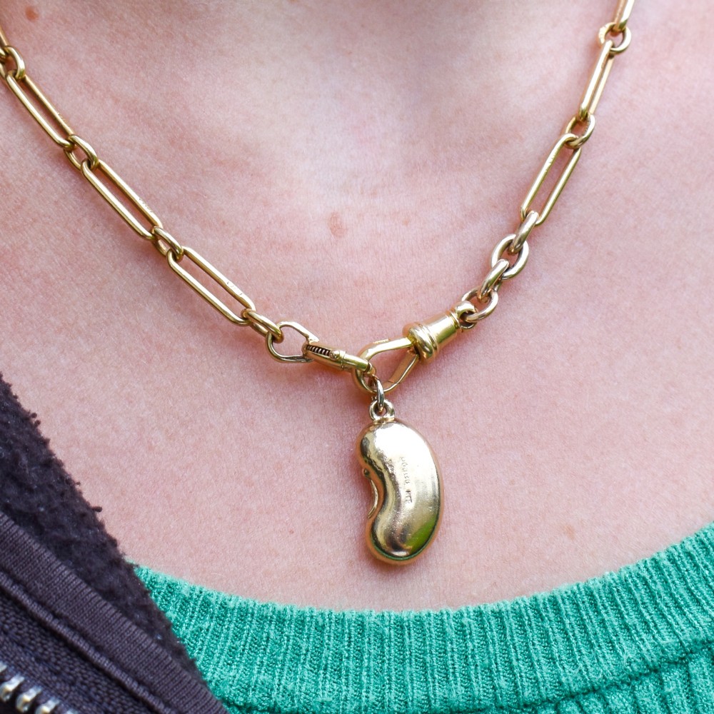 A smooth, polished 9ct yellow gold bean-shaped charm with an attached suspension jump ring. View X