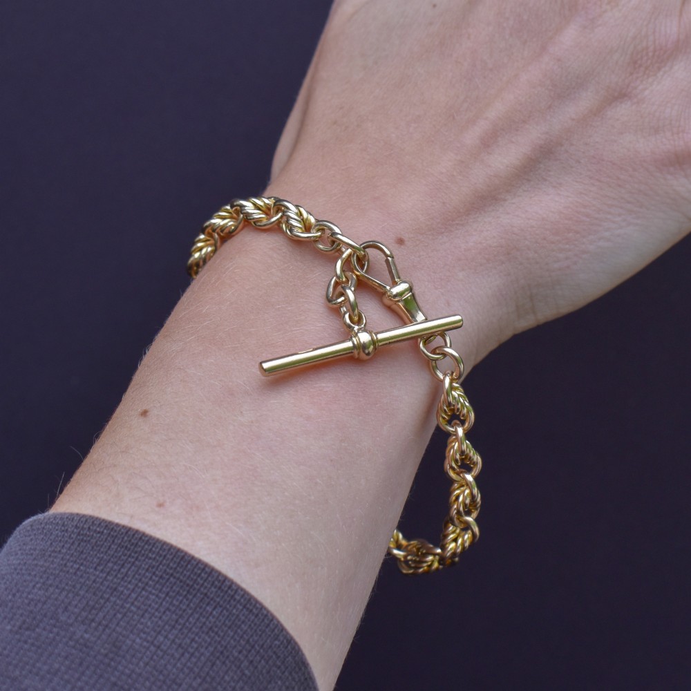 An antique 9ct yellow gold love knot chain bracelet featuring a swivel clasp and suspended T-bar detail. View IX