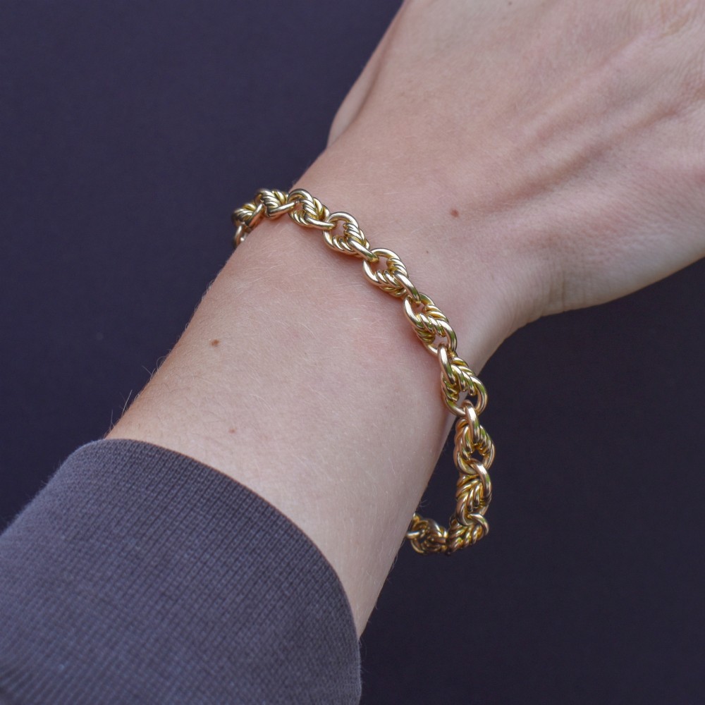 An antique 9ct yellow gold love knot chain bracelet featuring a swivel clasp and suspended T-bar detail. View X
