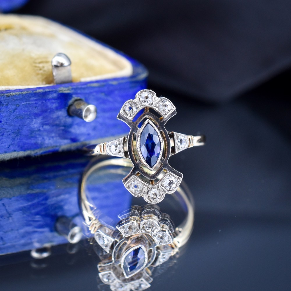 An Art Deco gold ring featuring a central marquise-cut blue sapphire framed by an intricate openwork diamond-set navette halo. View IV