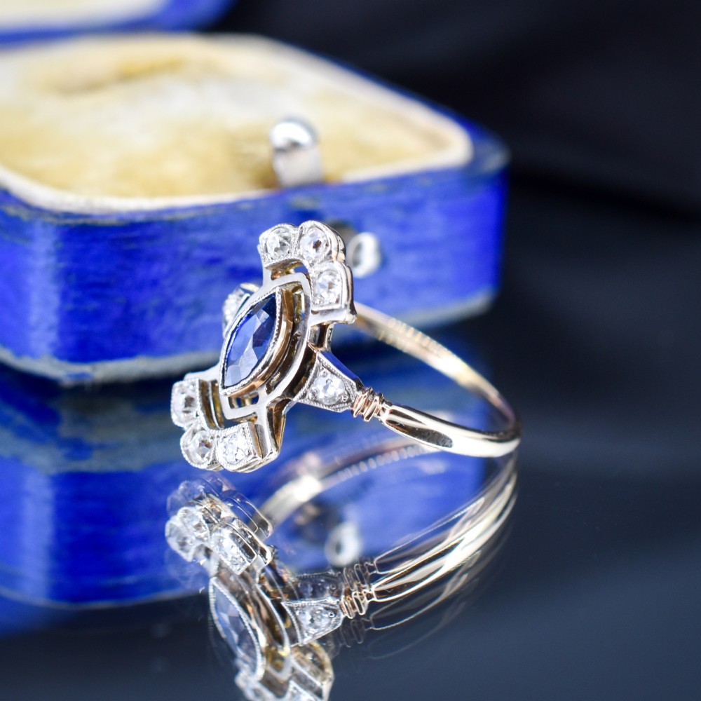 An Art Deco gold ring featuring a central marquise-cut blue sapphire framed by an intricate openwork diamond-set navette halo. View VI