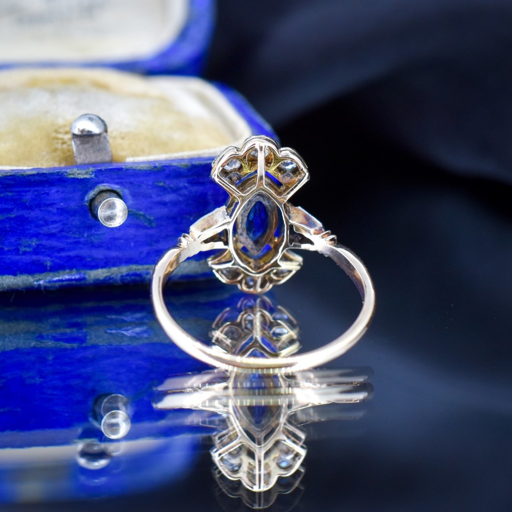 An Art Deco gold ring featuring a central marquise-cut blue sapphire framed by an intricate openwork diamond-set navette halo. View VII