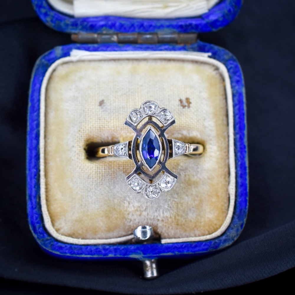 An Art Deco gold ring featuring a central marquise-cut blue sapphire framed by an intricate openwork diamond-set navette halo.
