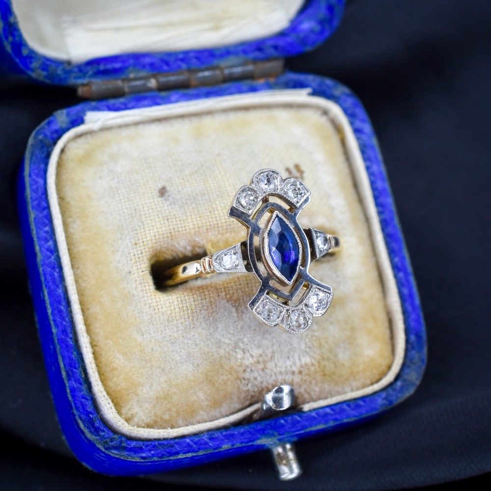 An Art Deco gold ring featuring a central marquise-cut blue sapphire framed by an intricate openwork diamond-set navette halo. View VIII