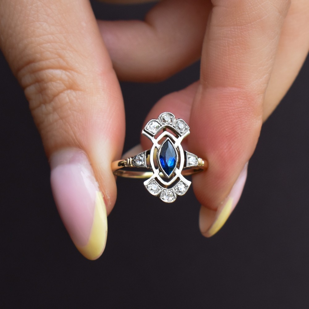 An Art Deco gold ring featuring a central marquise-cut blue sapphire framed by an intricate openwork diamond-set navette halo. View IX
