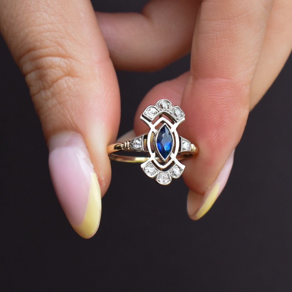 An Art Deco gold ring featuring a central marquise-cut blue sapphire framed by an intricate openwork diamond-set navette halo. View X