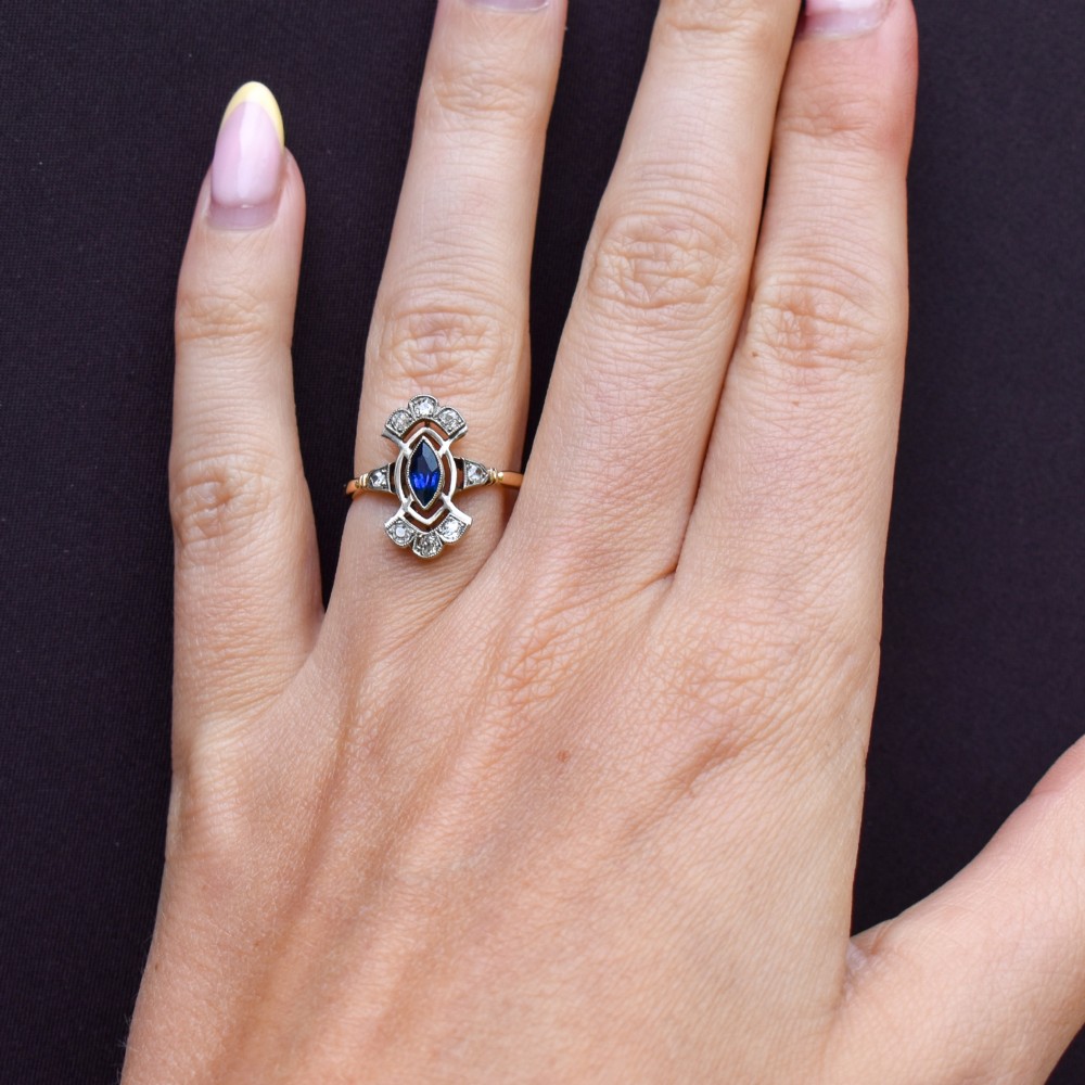 An Art Deco gold ring featuring a central marquise-cut blue sapphire framed by an intricate openwork diamond-set navette halo. View XI