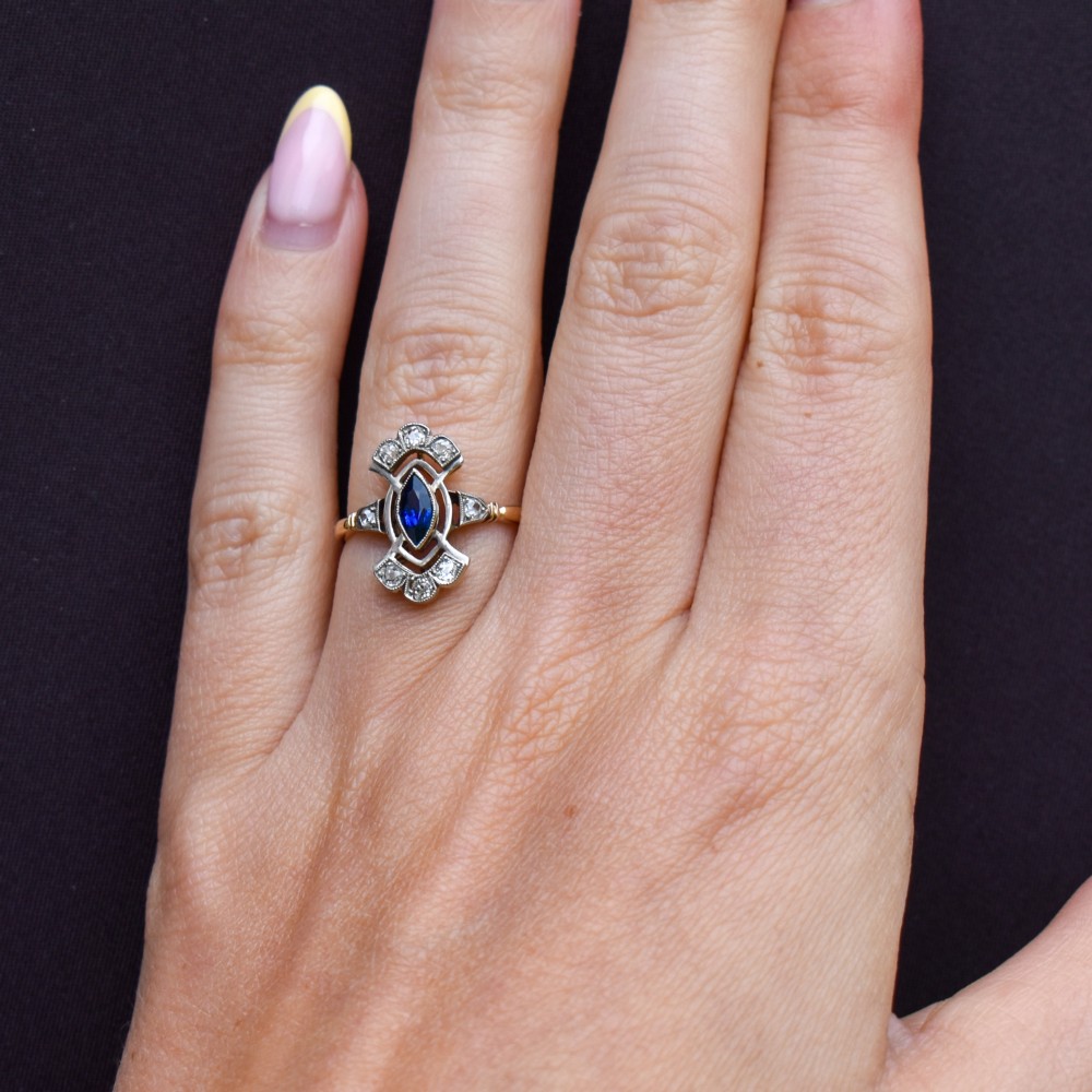 An Art Deco gold ring featuring a central marquise-cut blue sapphire framed by an intricate openwork diamond-set navette halo. View XII