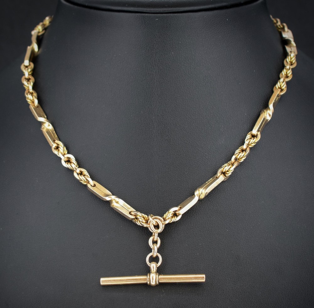 A 9ct yellow gold double Albert chain necklace with love knot links and a central T-bar drop displayed on a black bust.