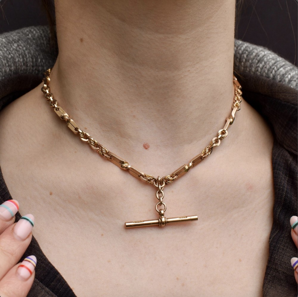 A 9ct yellow gold double Albert chain necklace with love knot links and a central T-bar drop displayed on a black bust. View II