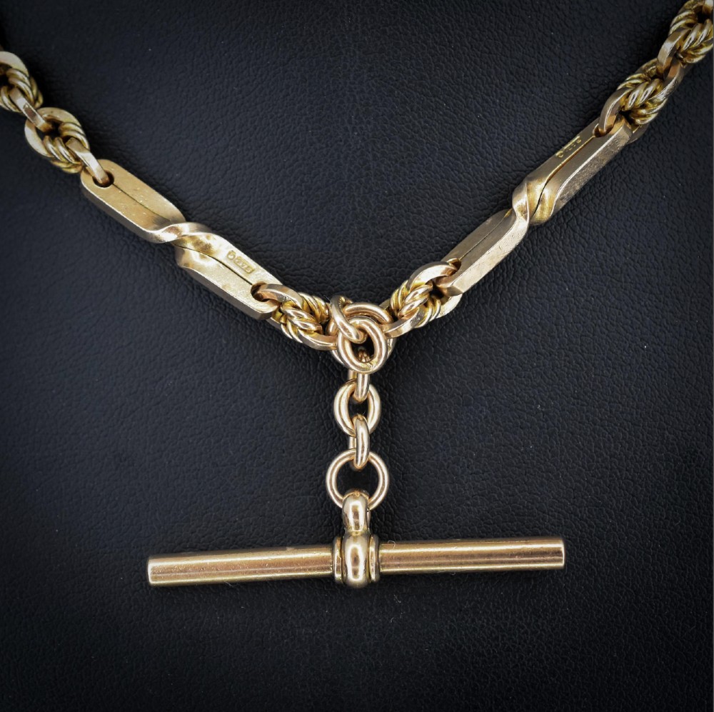 A 9ct yellow gold double Albert chain necklace with love knot links and a central T-bar drop displayed on a black bust. View IV