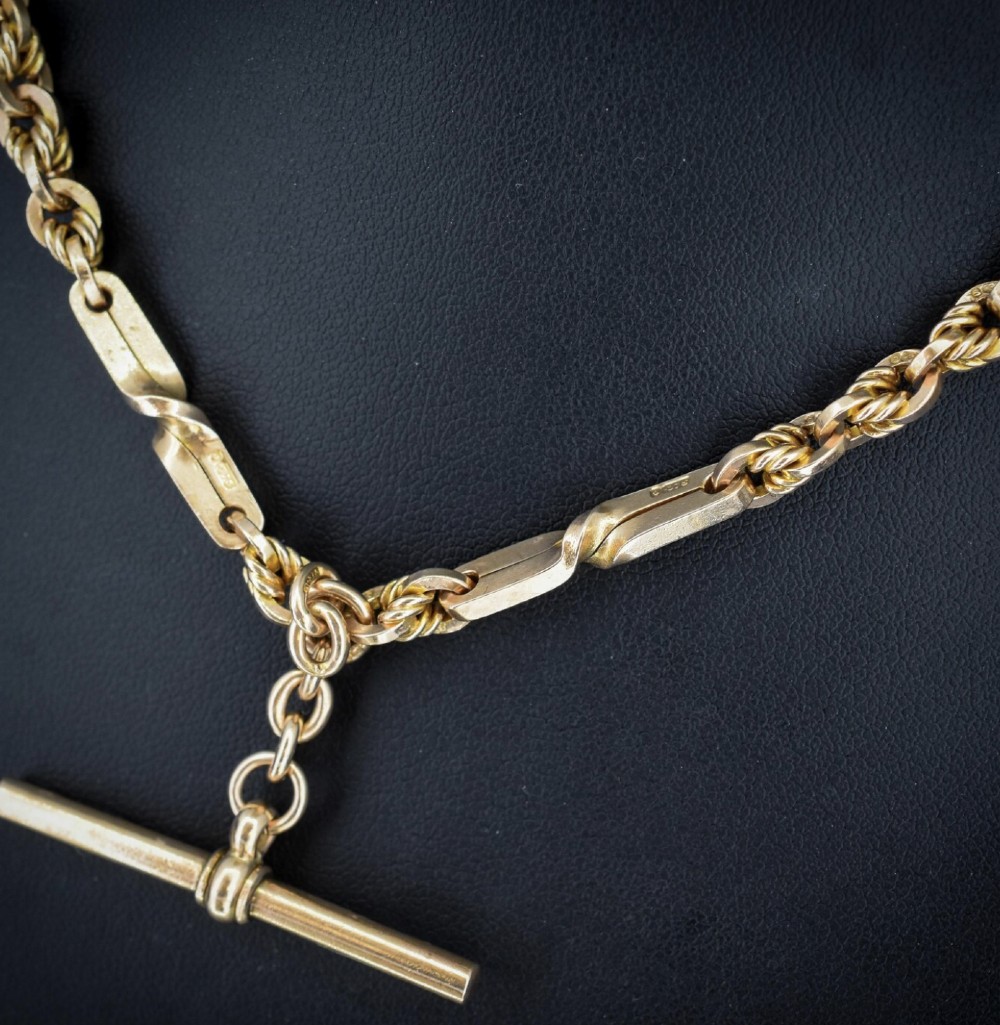 A 9ct yellow gold double Albert chain necklace with love knot links and a central T-bar drop displayed on a black bust. View V