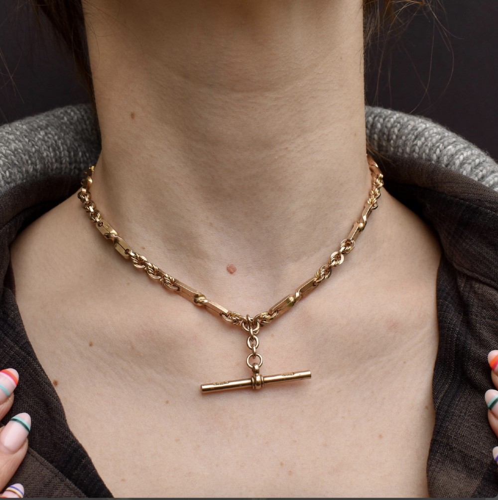 A 9ct yellow gold double Albert chain necklace with love knot links and a central T-bar drop displayed on a black bust. View X