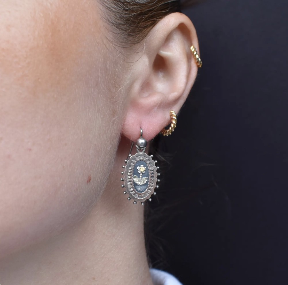 A pair of oval Victorian sterling silver drop earrings featuring central engraved flowers, scalloped inner borders, and beaded outer rims. View II