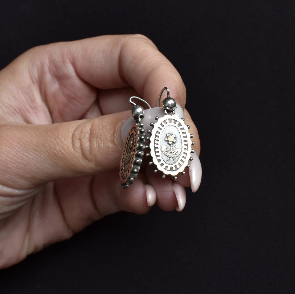 A pair of oval Victorian sterling silver drop earrings featuring central engraved flowers, scalloped inner borders, and beaded outer rims. View IV
