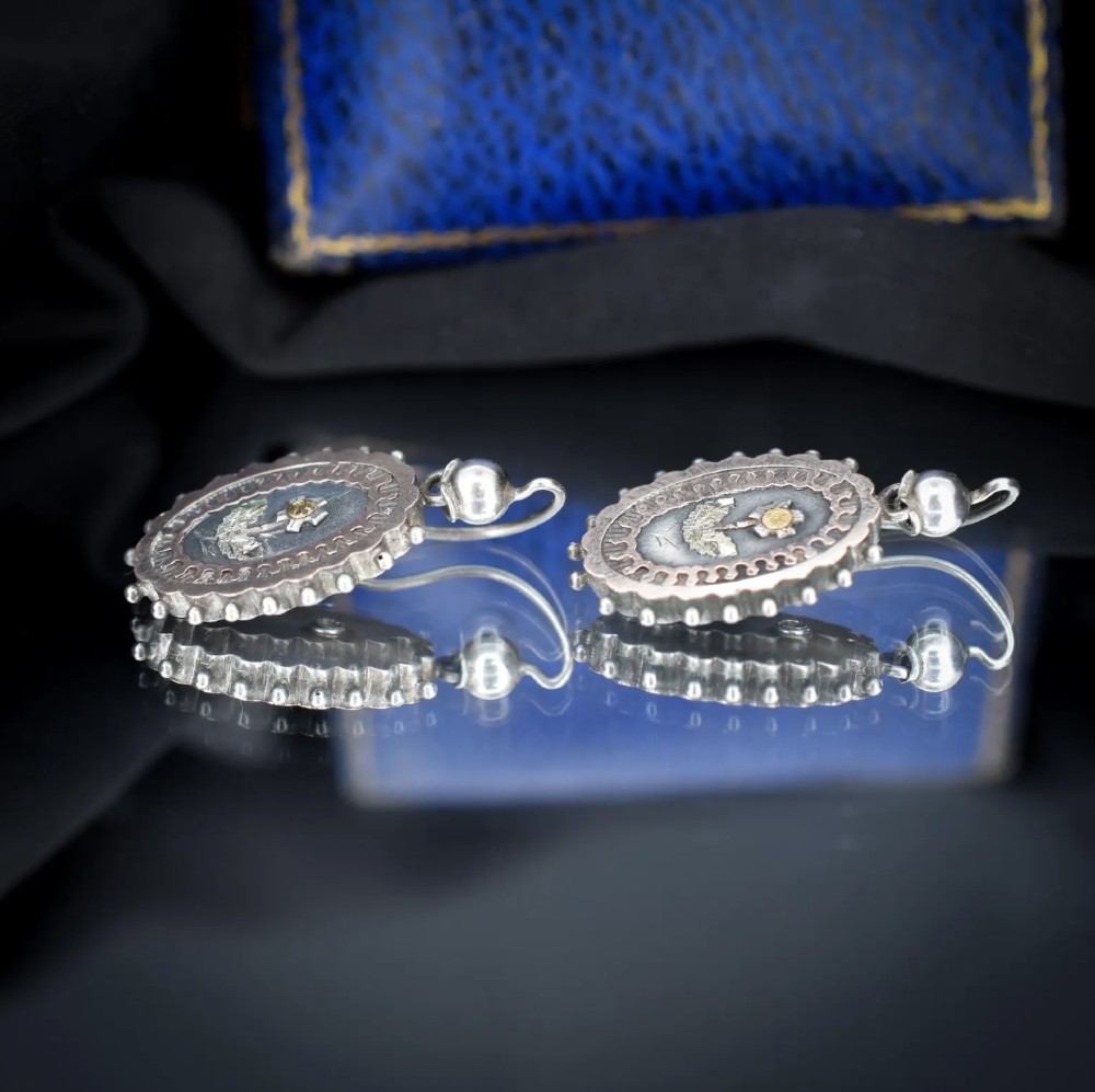 A pair of oval Victorian sterling silver drop earrings featuring central engraved flowers, scalloped inner borders, and beaded outer rims. View VII