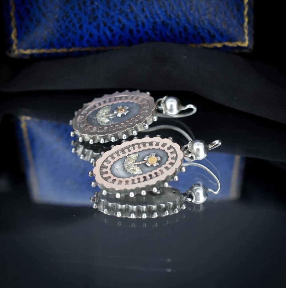 A pair of oval Victorian sterling silver drop earrings featuring central engraved flowers, scalloped inner borders, and beaded outer rims. View VIII
