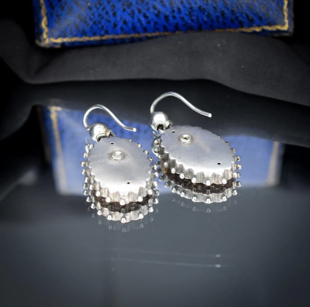 A pair of oval Victorian sterling silver drop earrings featuring central engraved flowers, scalloped inner borders, and beaded outer rims. View IX
