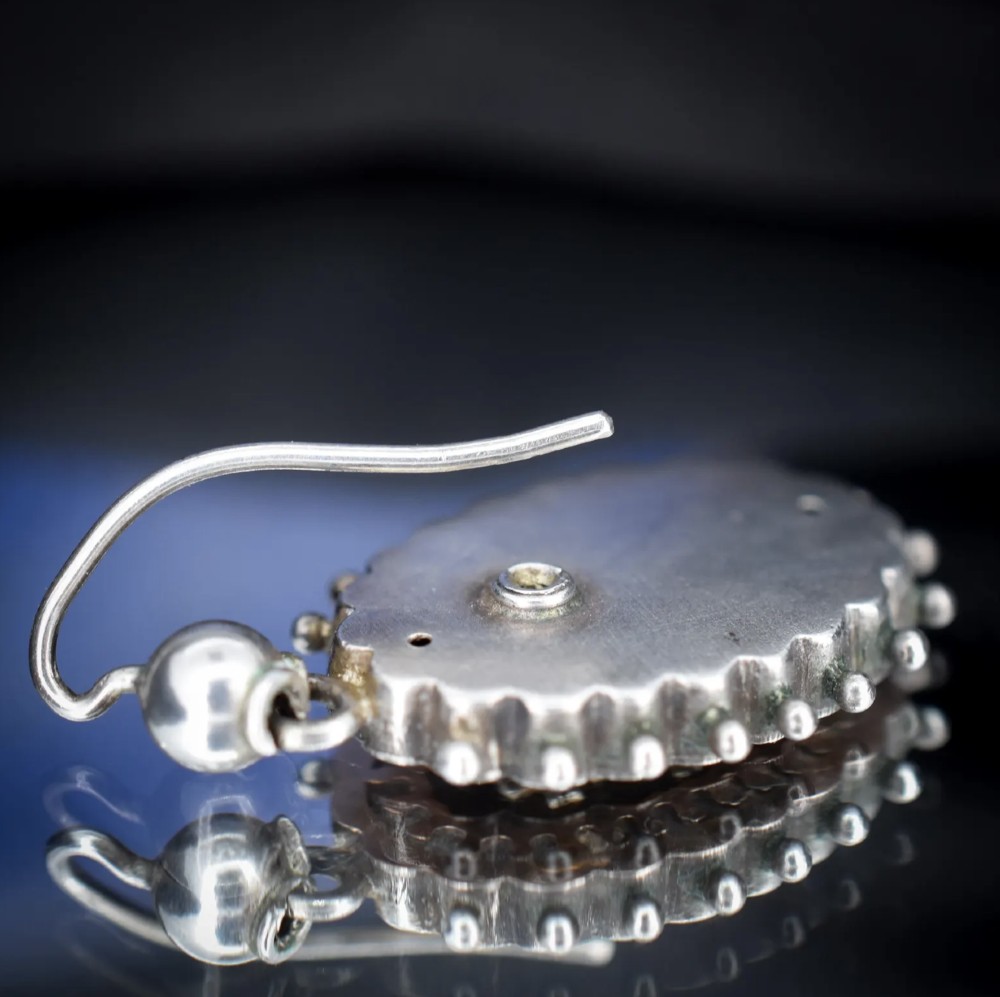 A pair of oval Victorian sterling silver drop earrings featuring central engraved flowers, scalloped inner borders, and beaded outer rims. View X