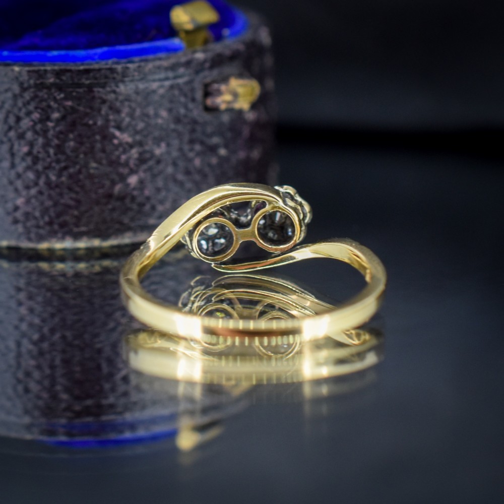 An antique 18ct yellow gold crossover ring featuring two diamond cluster flowers set in white metal on sweeping twist shoulders. View IV