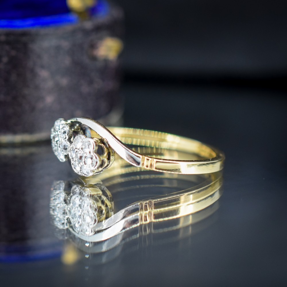 An antique 18ct yellow gold crossover ring featuring two diamond cluster flowers set in white metal on sweeping twist shoulders. View V