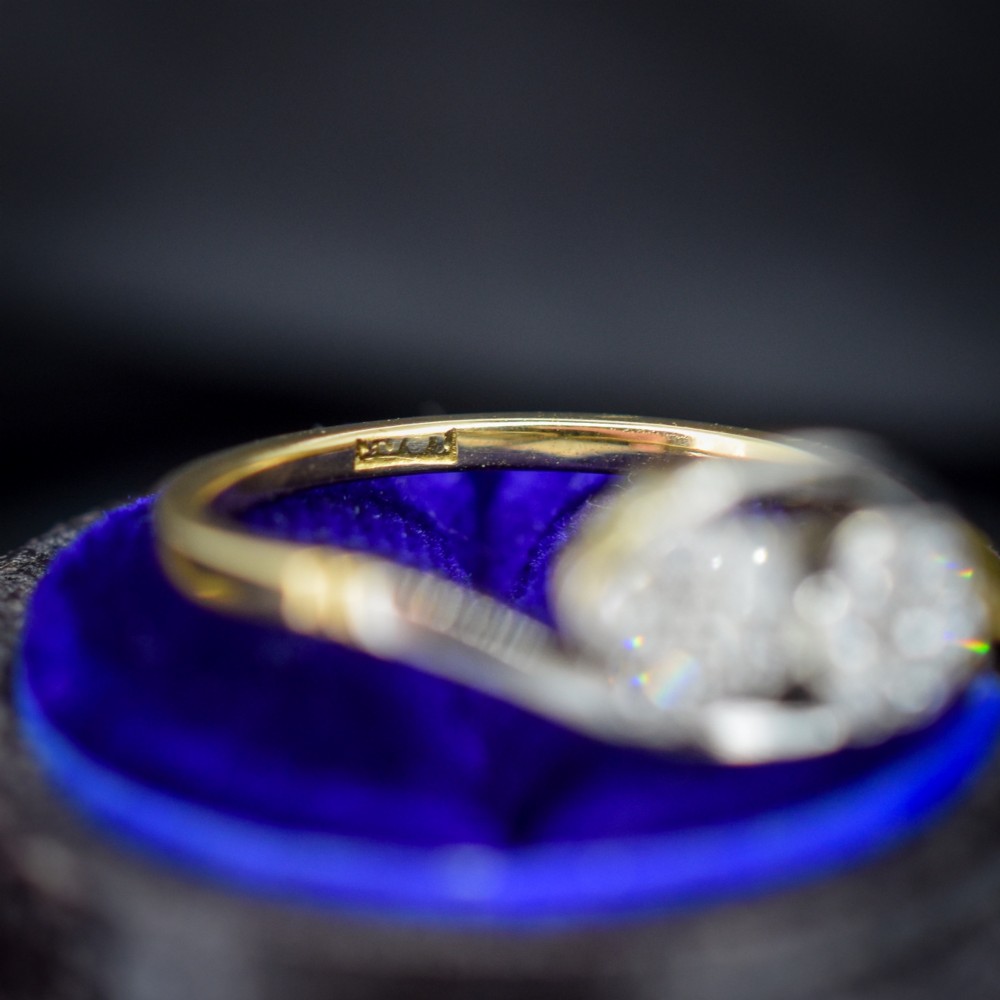An antique 18ct yellow gold crossover ring featuring two diamond cluster flowers set in white metal on sweeping twist shoulders. View VI