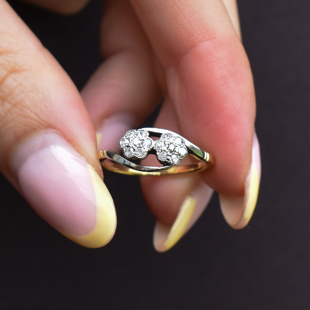 An antique 18ct yellow gold crossover ring featuring two diamond cluster flowers set in white metal on sweeping twist shoulders. View VII