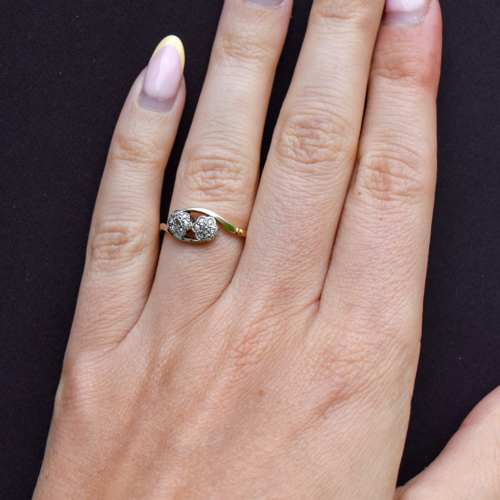 An antique 18ct yellow gold crossover ring featuring two diamond cluster flowers set in white metal on sweeping twist shoulders. View IX